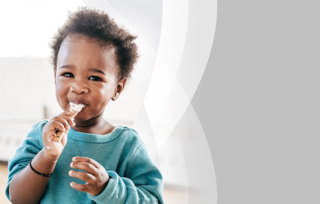 Child grinning while licking a spoon.