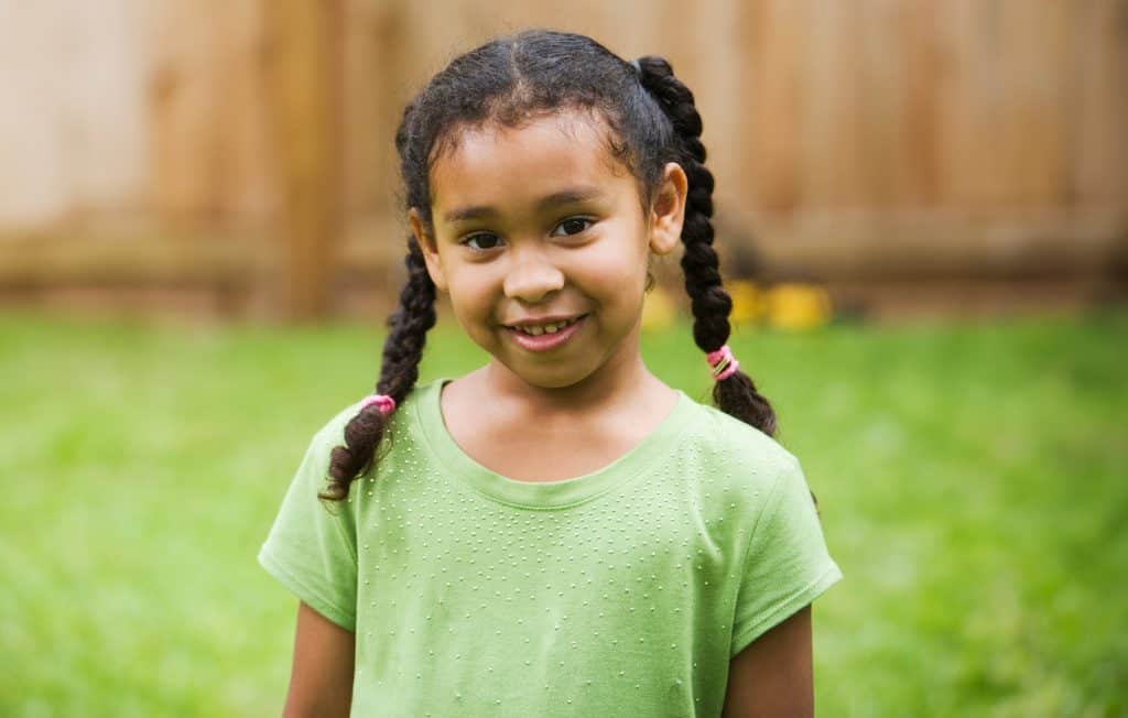 A young girl with braided hair smiles warmly, wearing a green top
